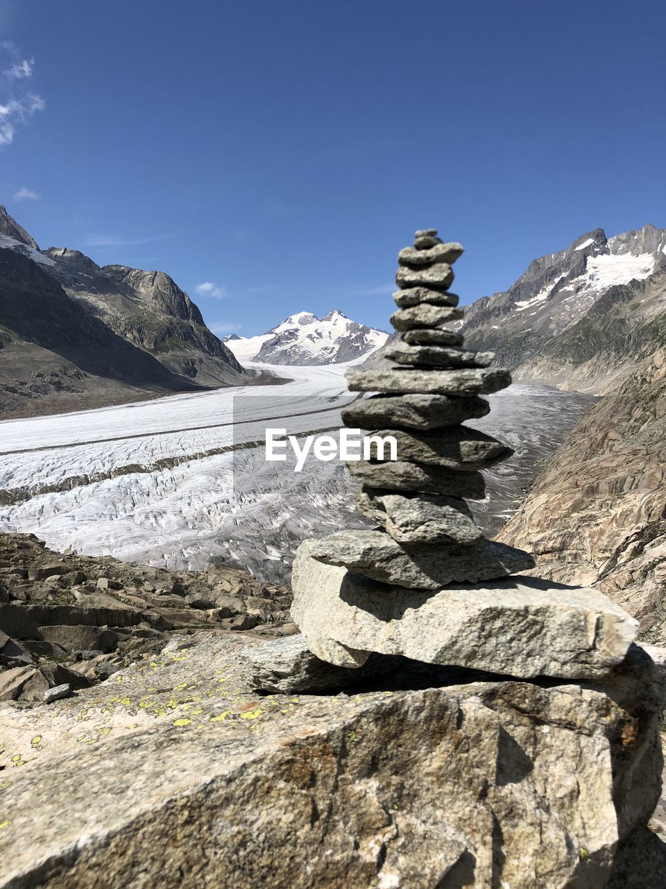 Stack of rocks on mountain against sky with glacier