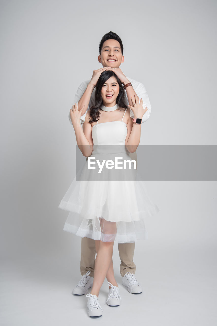 Full length portrait of smiling couple standing over gray background