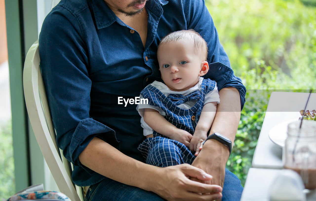 Midsection of father carrying cute son while sitting in cafe