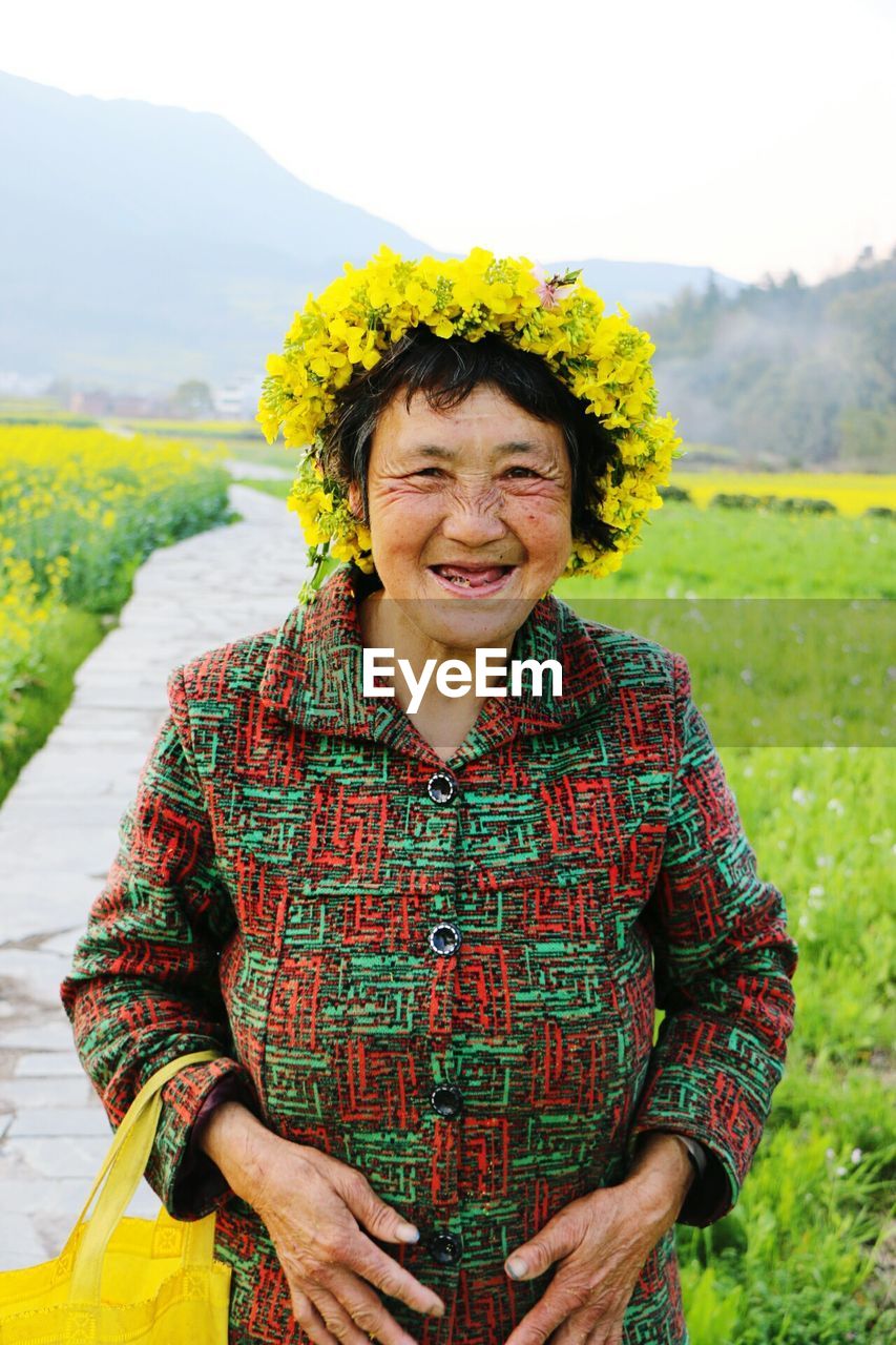 Portrait of happy senior woman wearing flower wreath on field