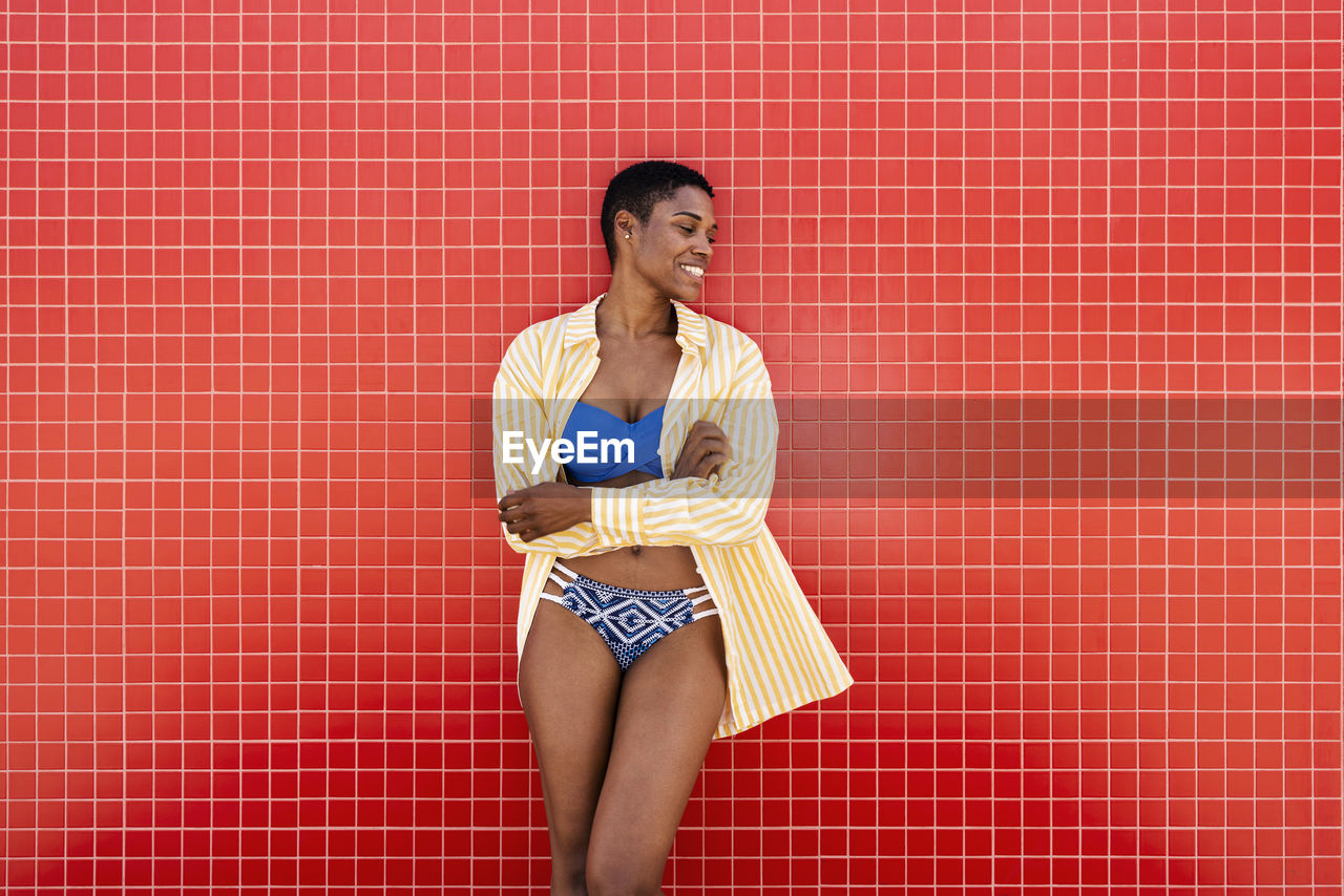 Smiling woman in bikini leaning on red wall