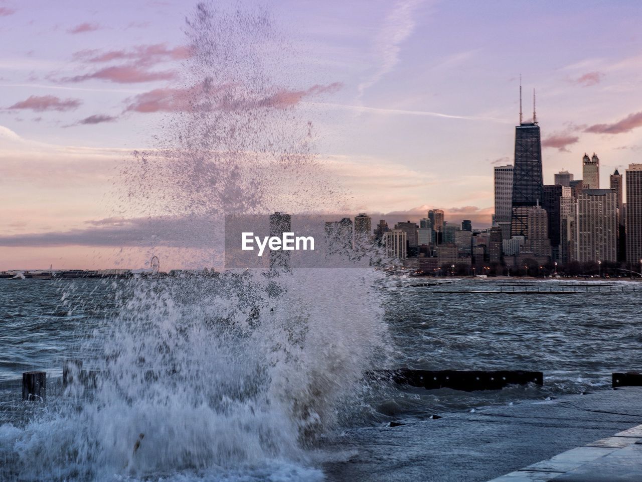 Water splashing in sea against sky at city during sunset