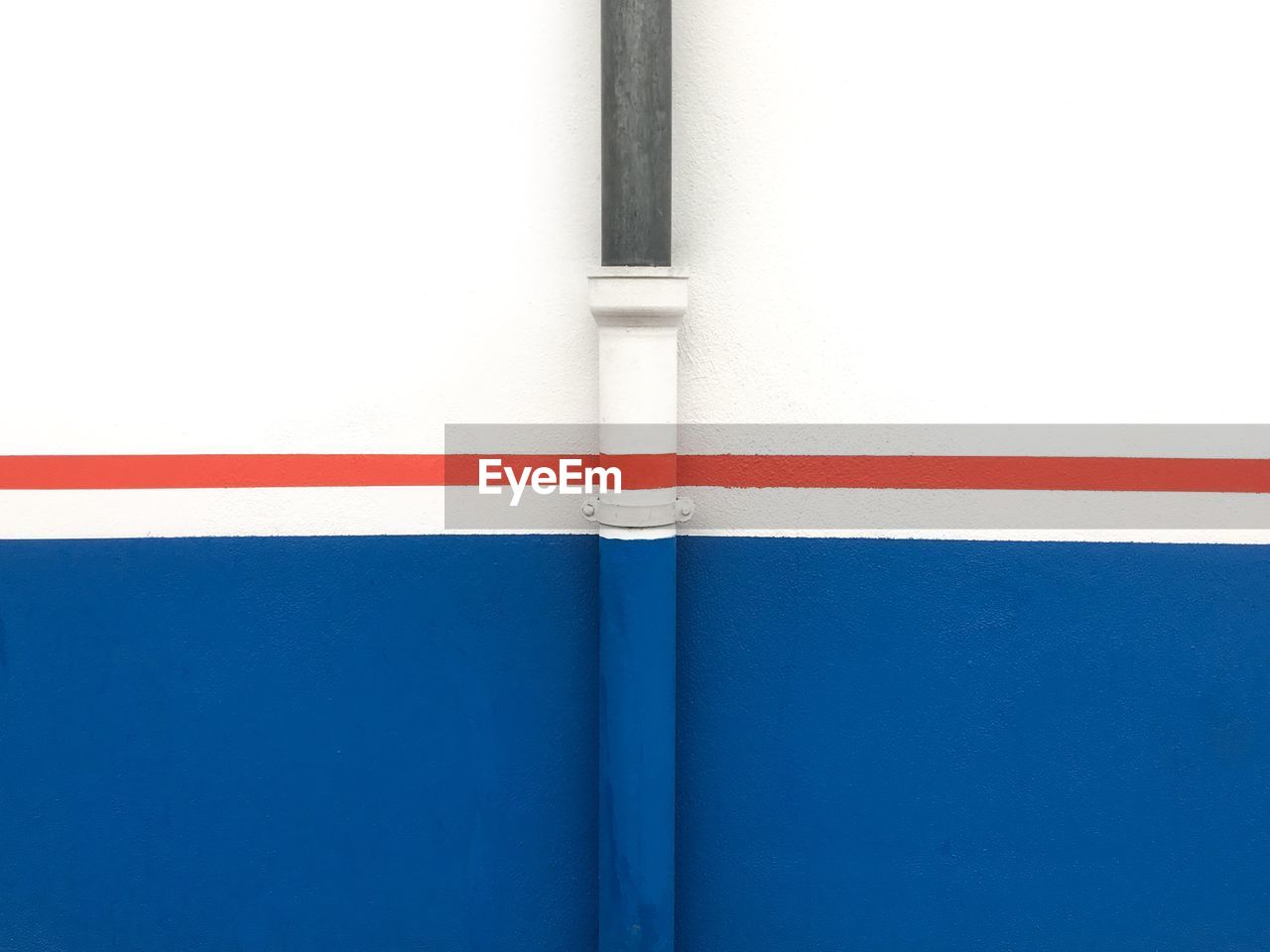 Full frame street shot of blue and white wall with a thin red line crossing and a pipe painted.