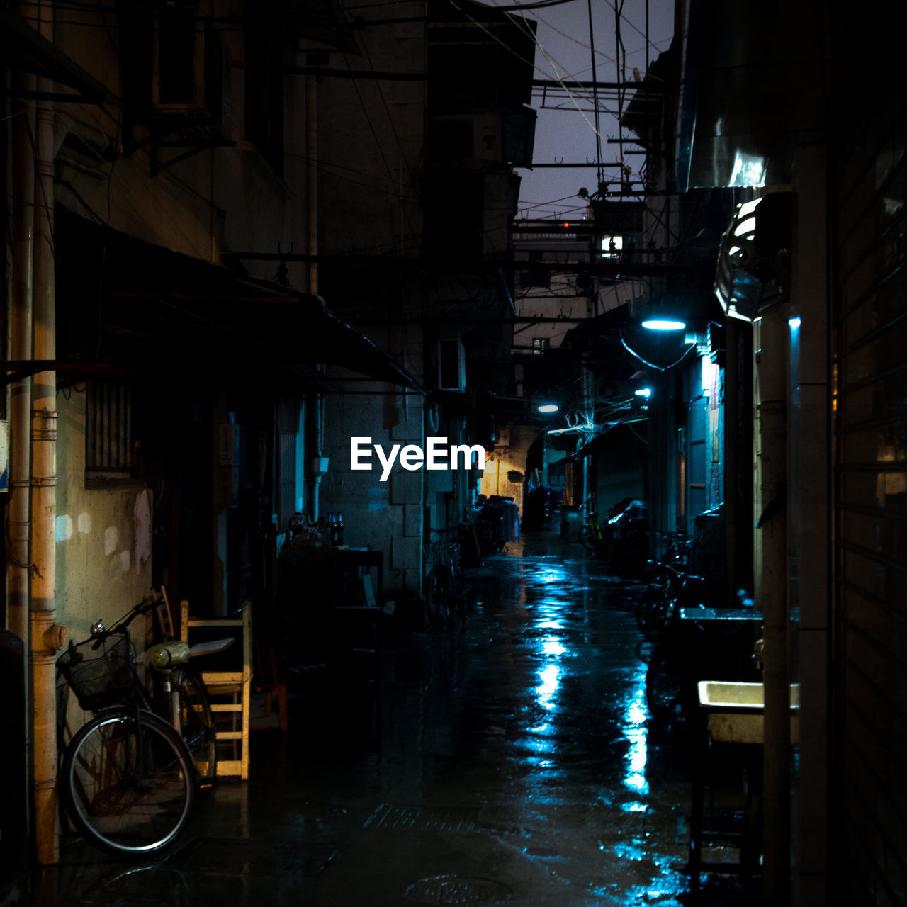 Wet street amidst illuminated buildings in city during rainy season