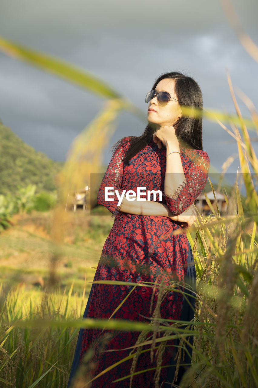 YOUNG WOMAN STANDING ON FIELD IN SUNLIGHT