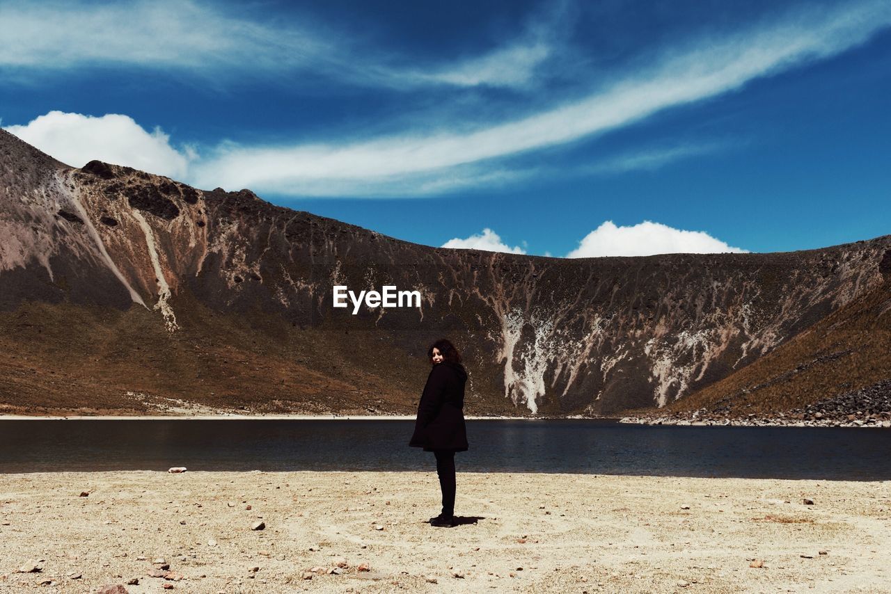 Woman standing by lake against mountain