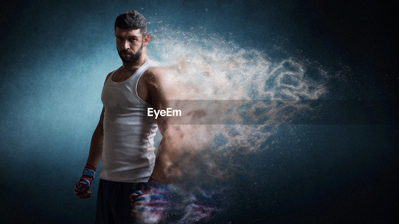 Digital composite image of dissolving boxer standing against blue background
