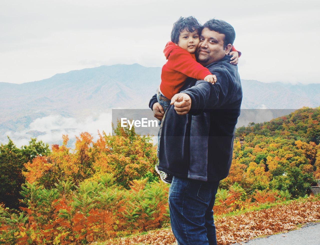 Portrait of man carrying son on road against mountains