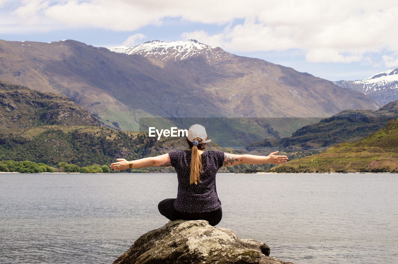 Rear view of man standing on rock by lake against mountains