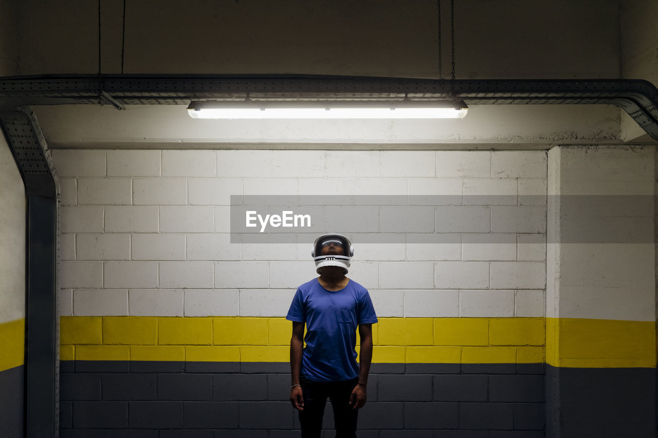 Young man wearing astronaut helmet standing in front of wall at underground walkway
