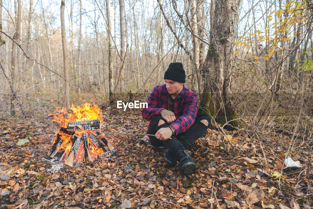 Full length of man sitting by campfire in forest during autumn