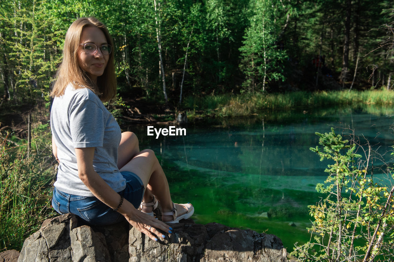 Woman sitting on rock by lake in forest