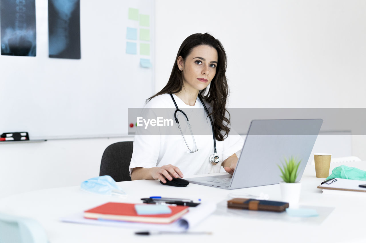 Confident female doctor working on desk in clinic