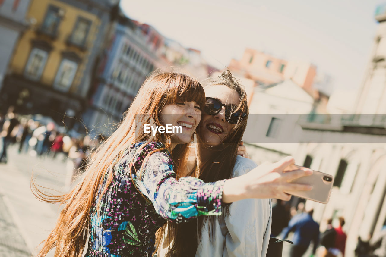 Cheerful friends doing selfie standing outdoors