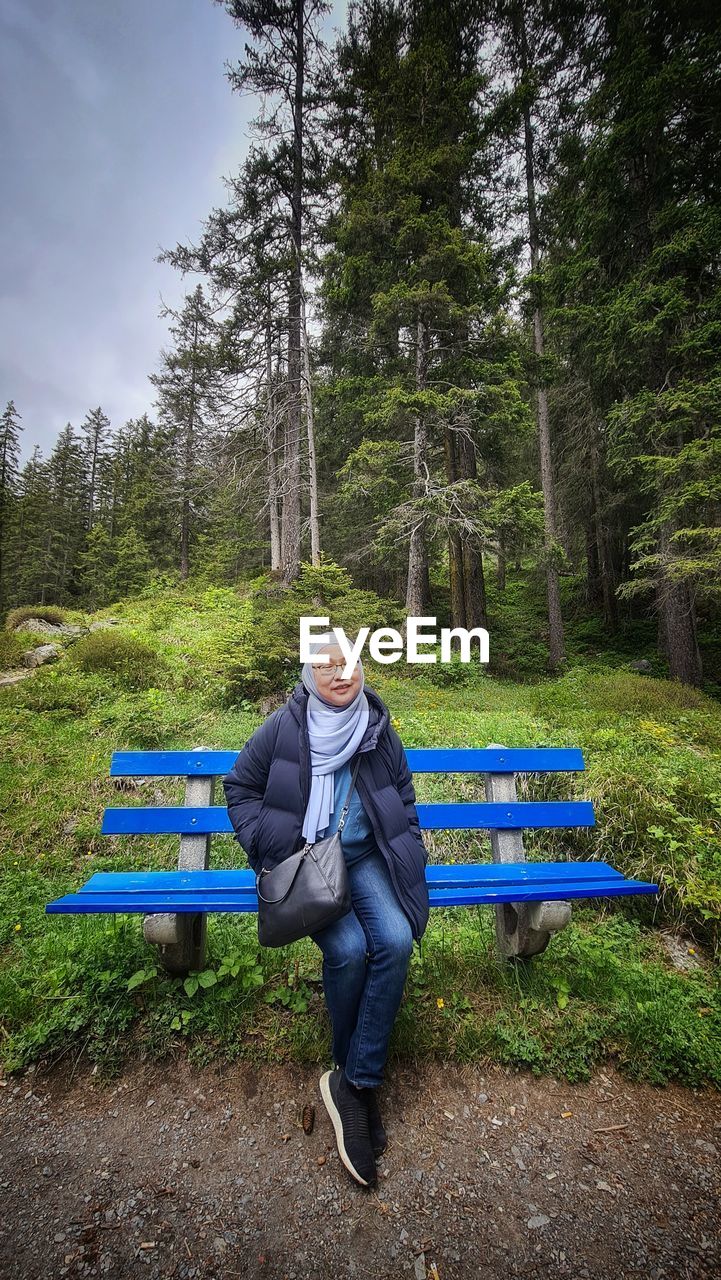 Front view of woman sitting on bench in forest