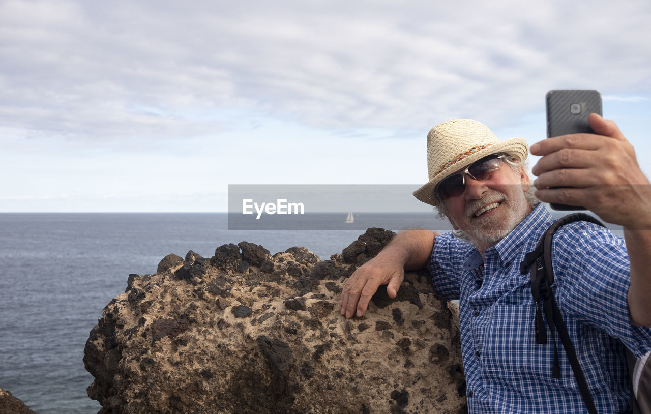 Senior man taking selfie against sea