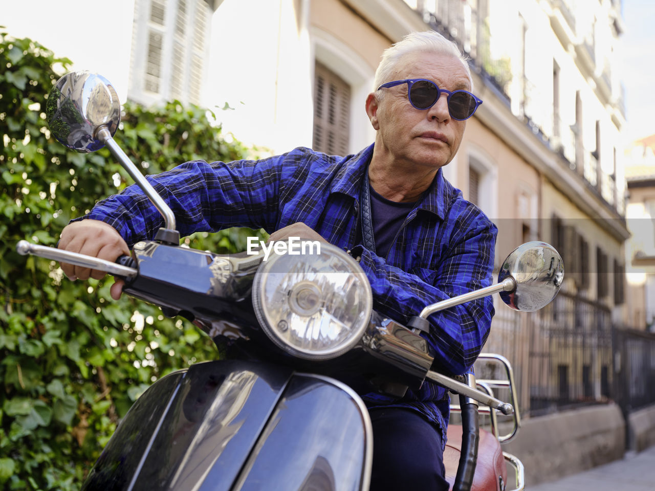 Low angle of smiling woman in vintage outfit sitting on retro motorbike and cheerfully looking away