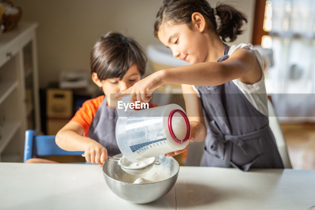 Two sisters wearing grey aprons sifting flour