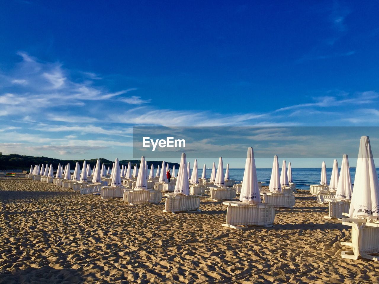 Closed parasols and lounge chairs at beach against blue sky