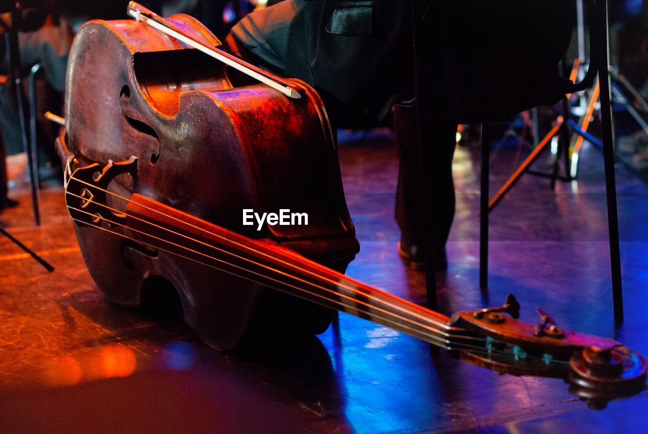 Low section of musician sitting by double bass on stage