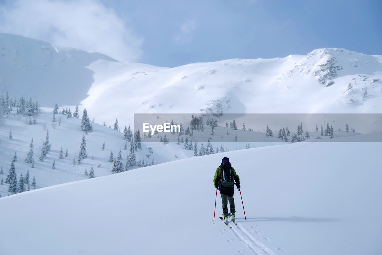 REAR VIEW OF PERSON SKIING ON SNOWCAPPED MOUNTAIN AGAINST MOUNTAINS