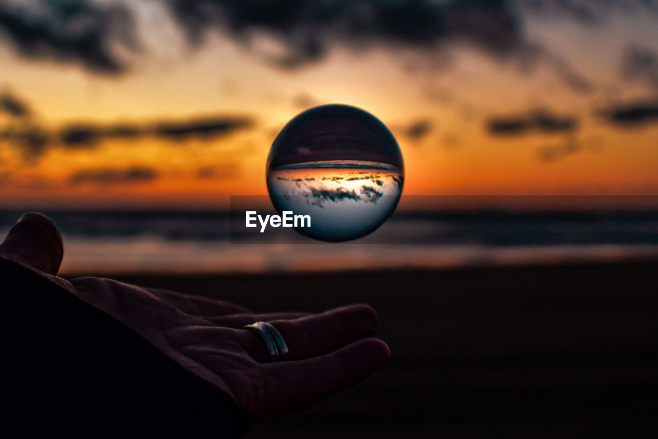 Close-up of hand against sea at sunset