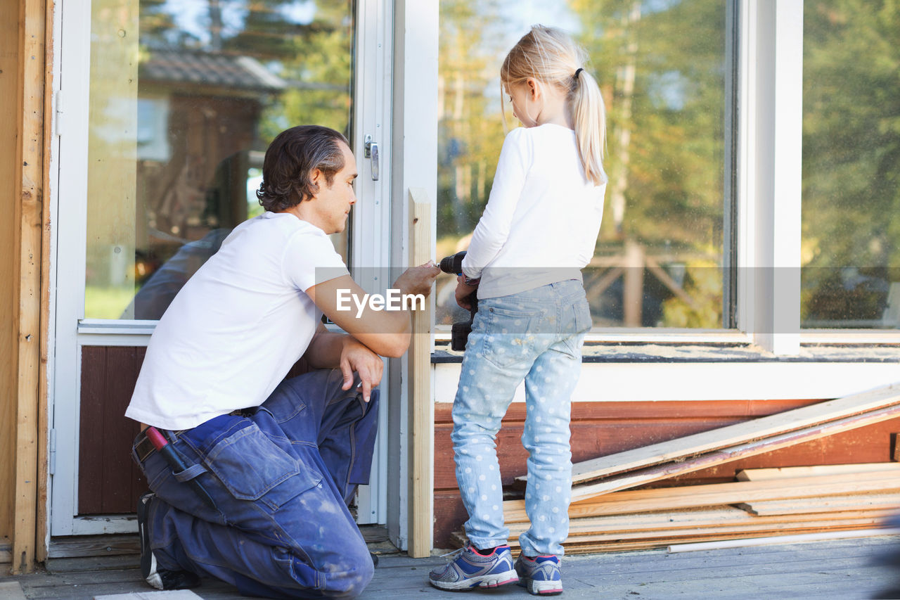 Father assisting girl in using cordless screwdriver on frame during home improvement