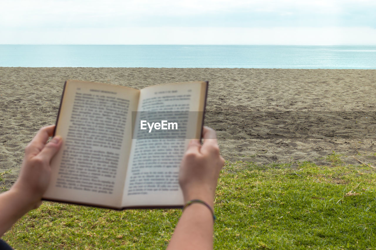 Midsection of person reading book at beach