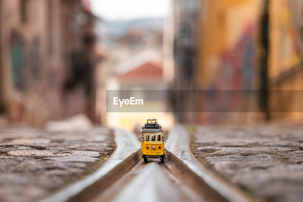 CLOSE-UP OF YELLOW TOY CAR ON WOOD BY BUILDING