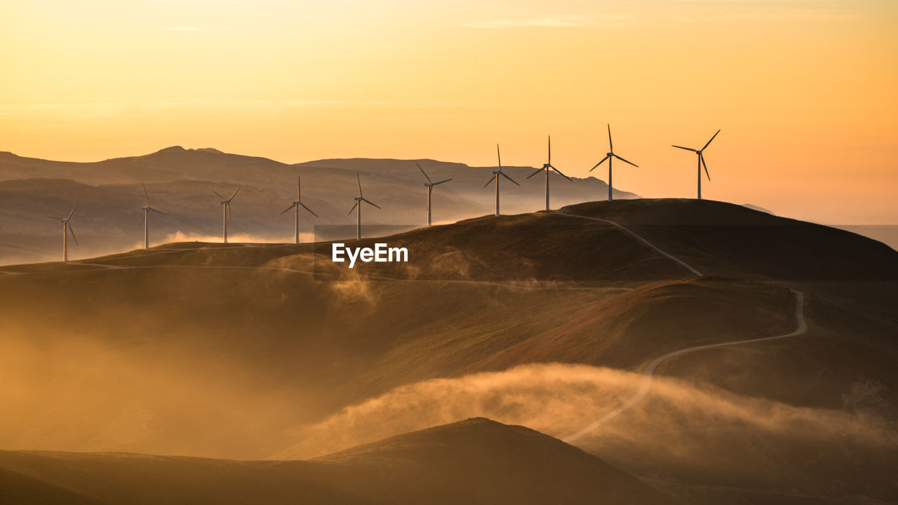 Low angle view of silhouette windmills on mountain against sky during sunset