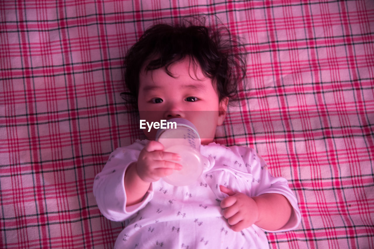 Close-up portrait of cute baby holding milk bottle while lying on blanket