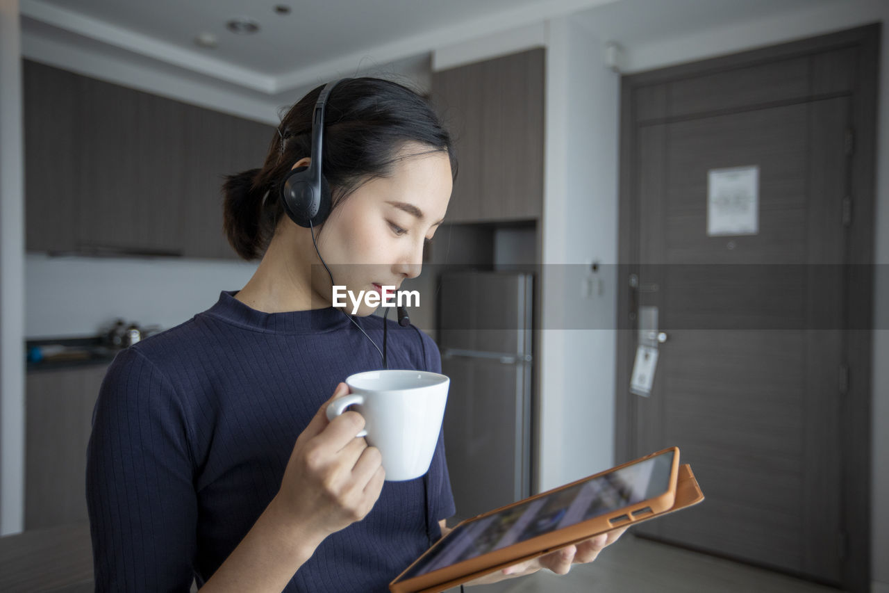 YOUNG WOMAN DRINKING COFFEE CUP IN KITCHEN