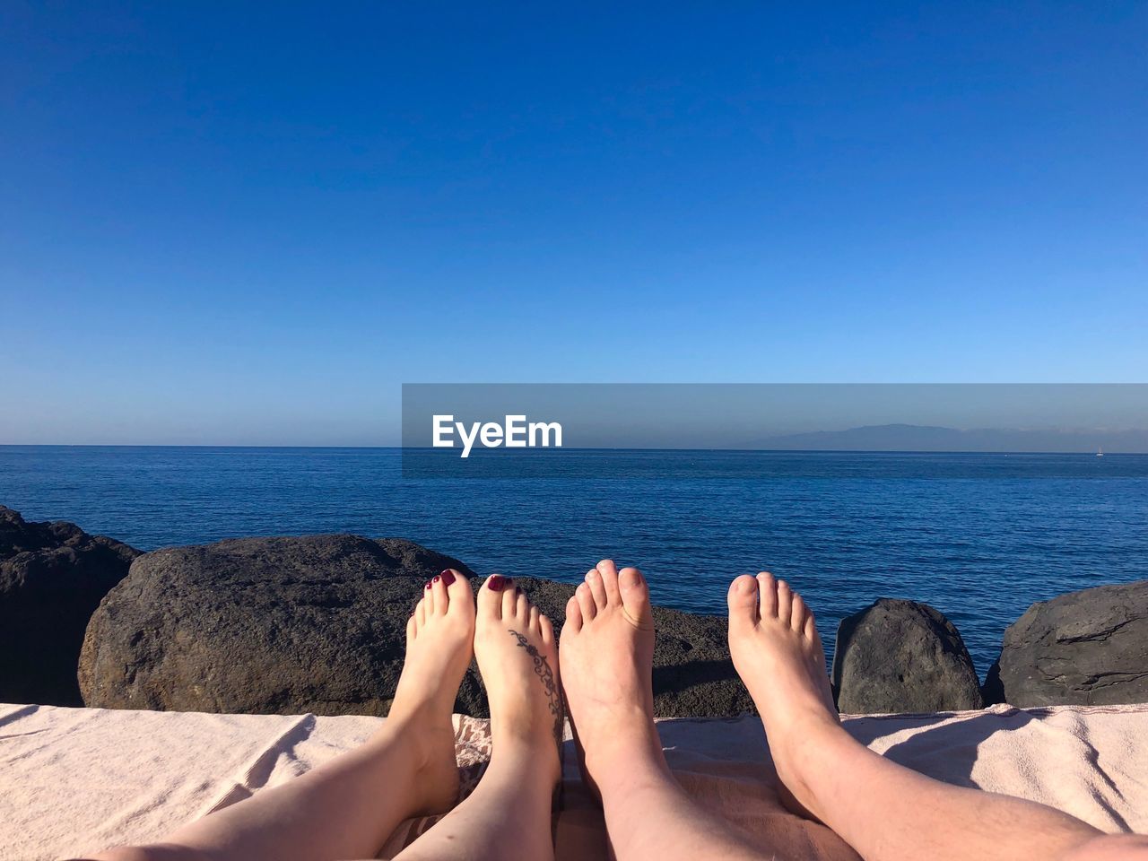 Low section of friends at beach against blue sky