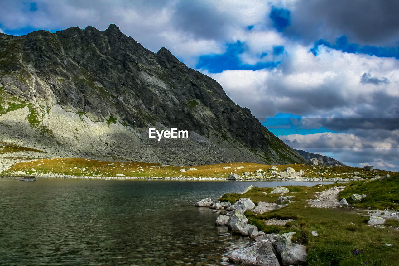 Scenic view of lake by mountain against cloudy sky