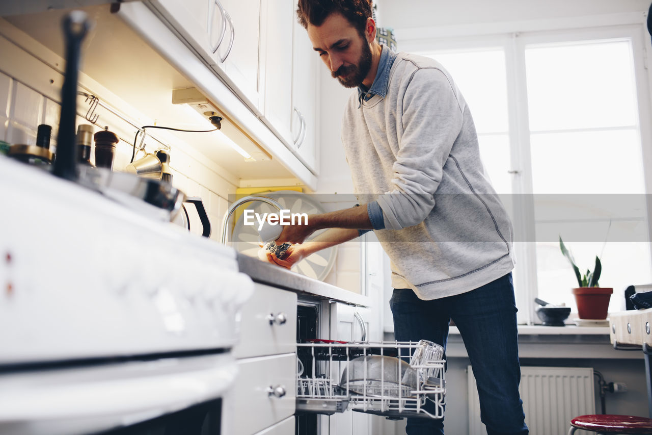 Man cleaning utensils in kitchen at home