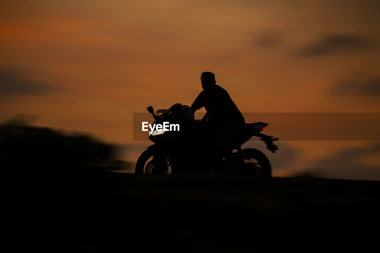 Silhouette man riding motorcycle against sky during sunset
