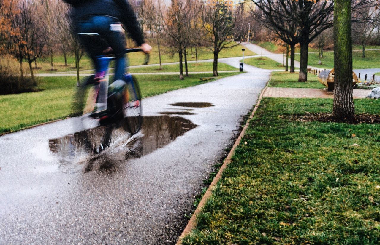 Blurred motion of man riding bicycle on wet street during rainy season