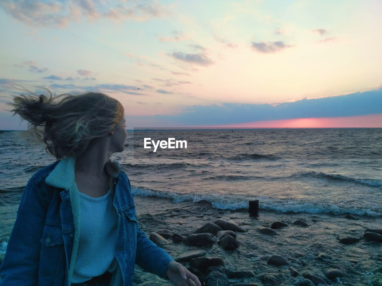 Woman standing at beach against sky during sunset