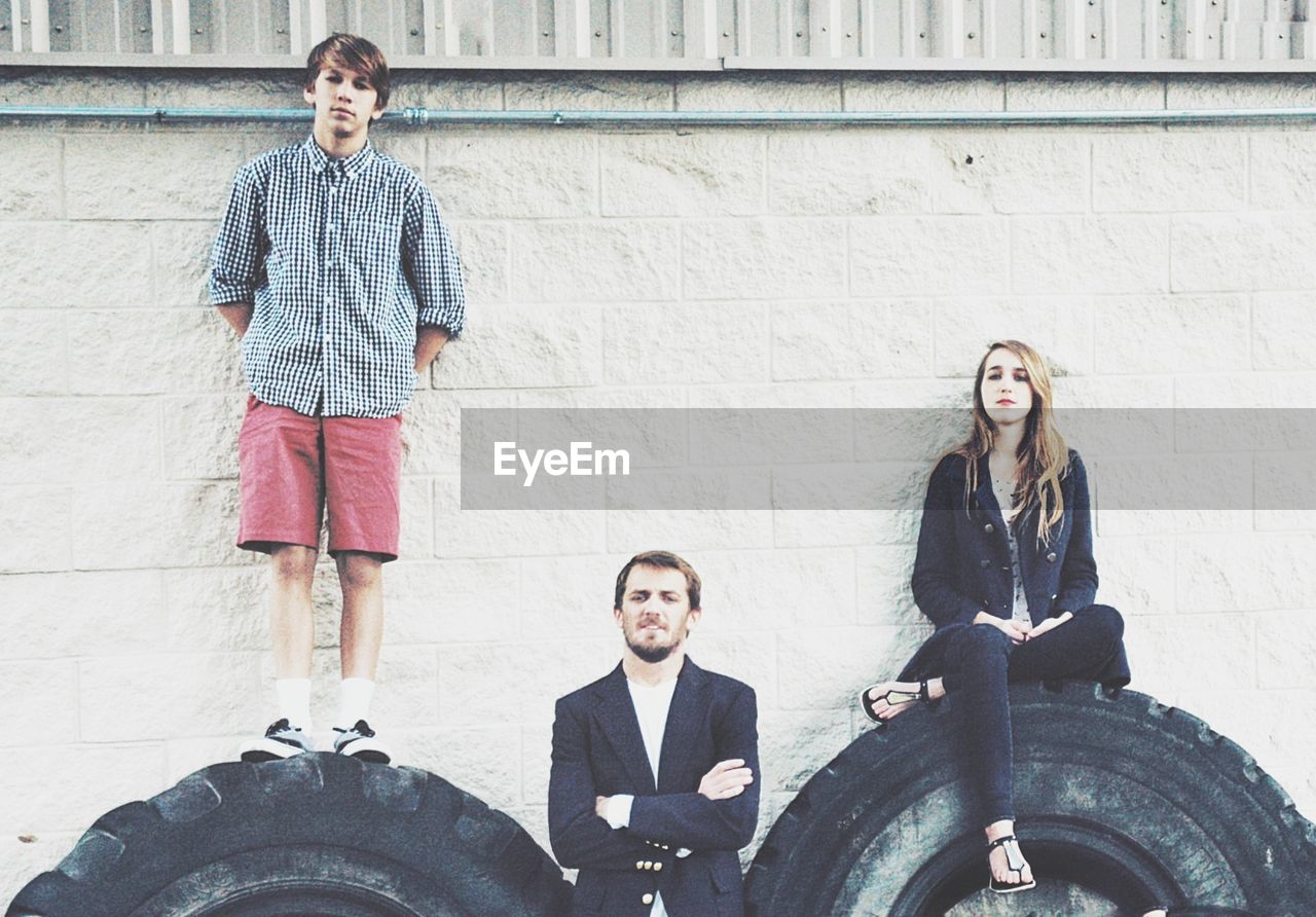 Portrait of friends standing on tire against wall