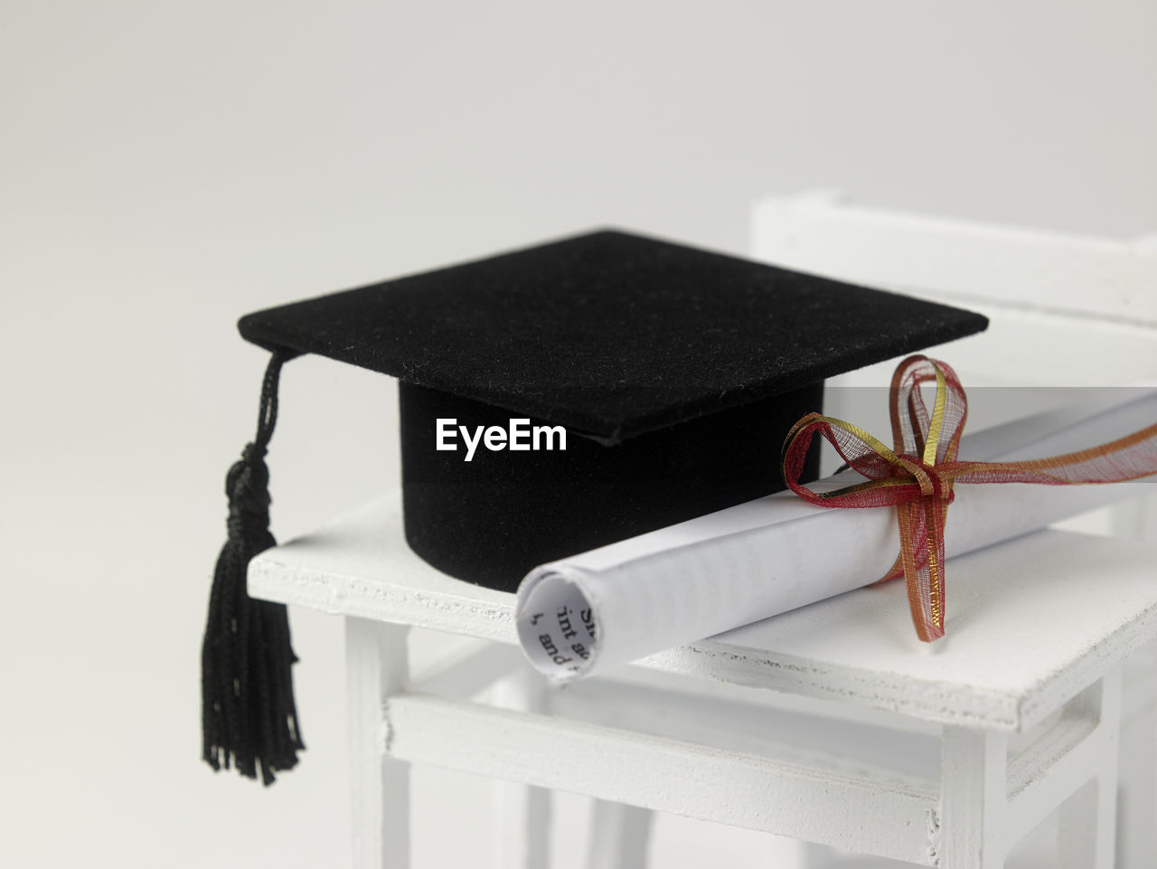 Mortarboard and diploma on table with chair against white background