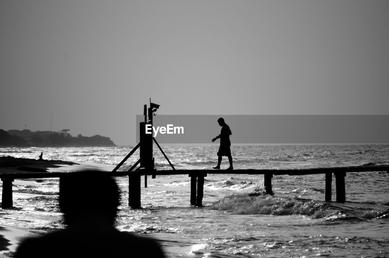 Silhouette man walking on pier over sea against clear sky