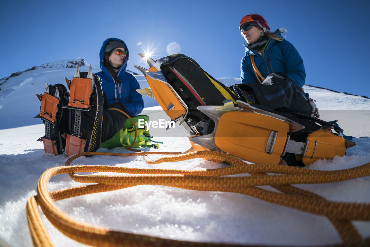 Two female mountaineers sit with their cramp-ons, discussing.