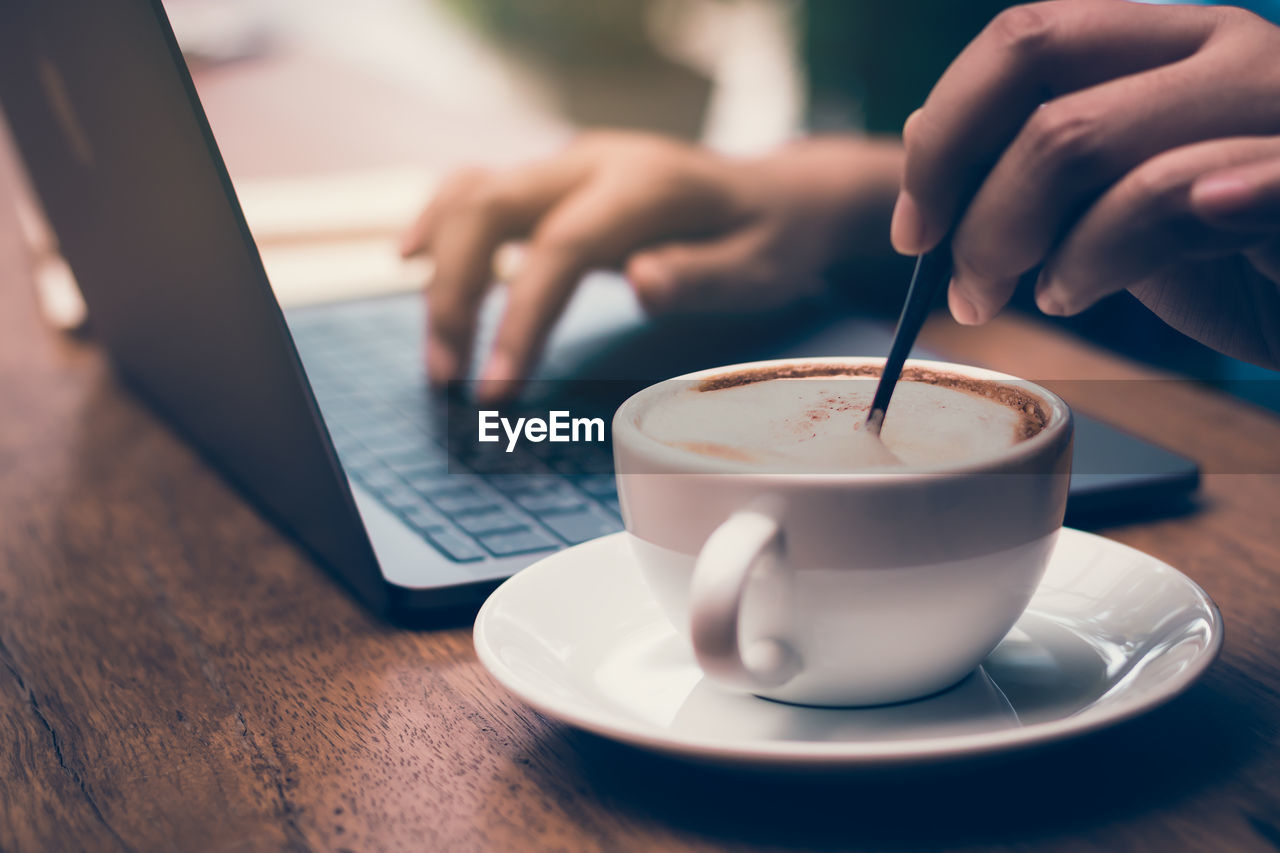 Cropped hand having coffee while using laptop at table