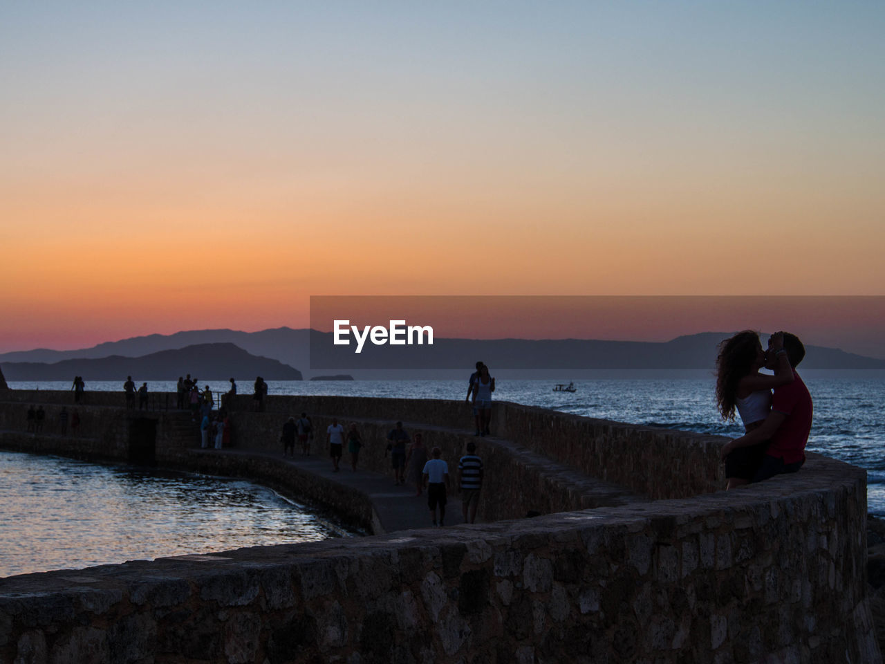 Couple kissing by sea against clear sky at dusk