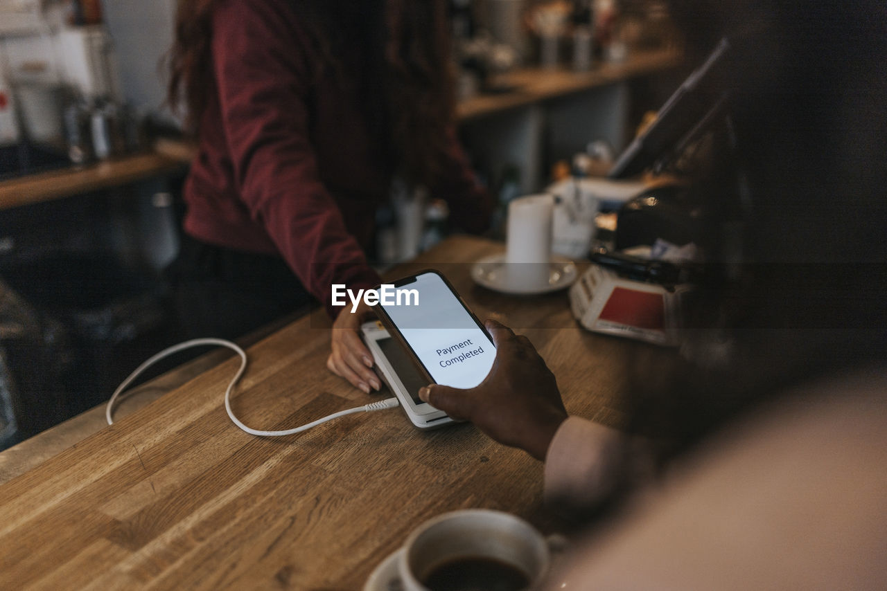 Hand of female customer making contactless payment through smart phone at checkout in cafe