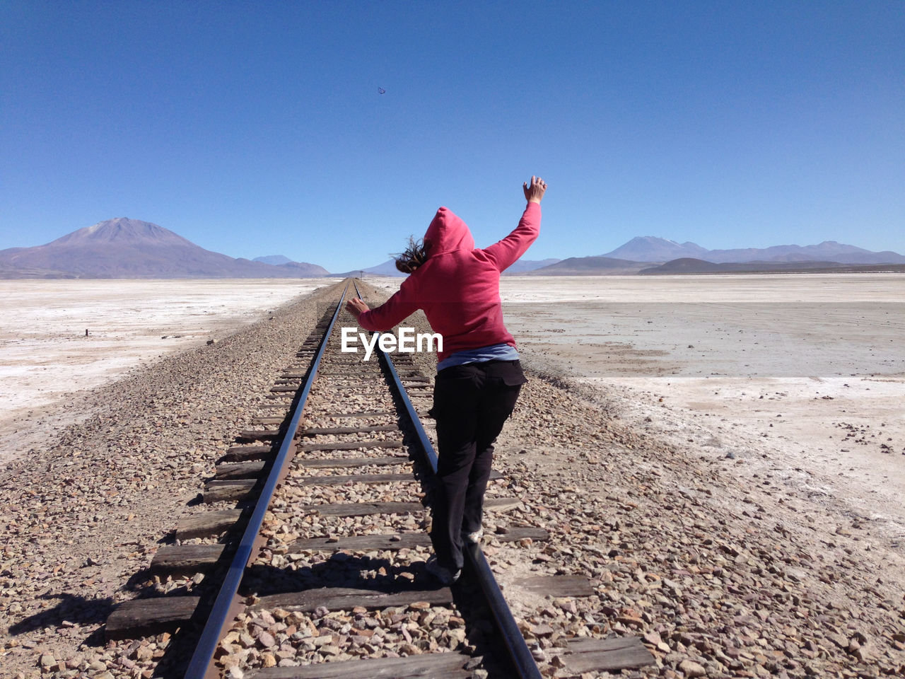 Rear view of woman walking on railroad tracks against sky