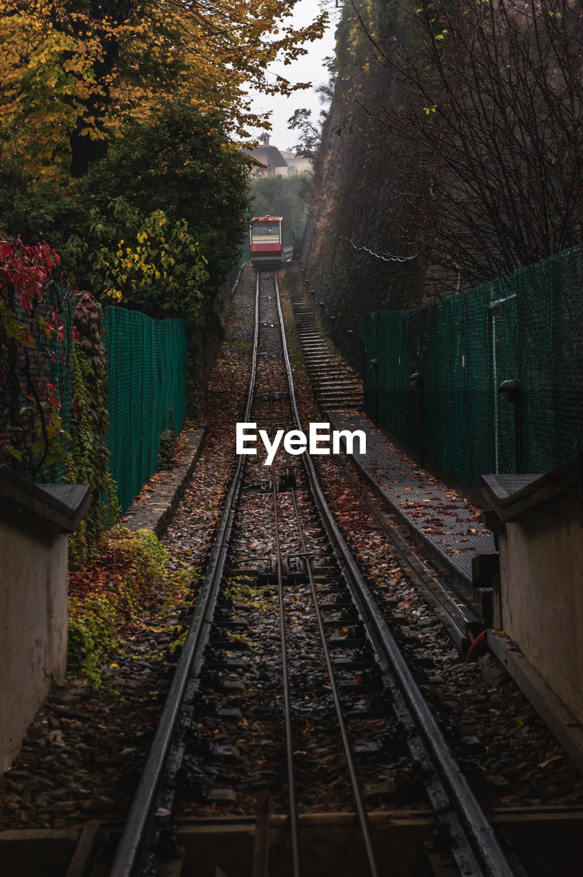 Railroad tracks along plants and trees with a funicular in a distance on a rainy autumn day