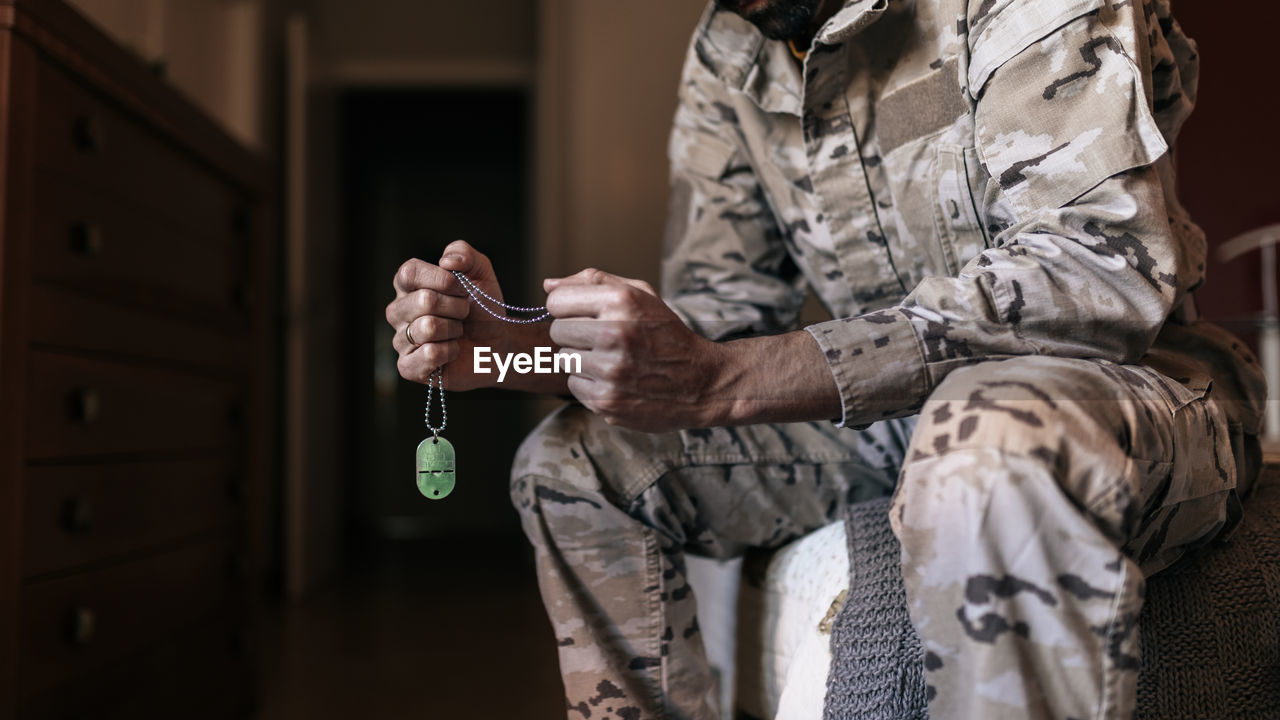 Low angle of a faceless soldier, holding the name badge, while preparing for military service at home.