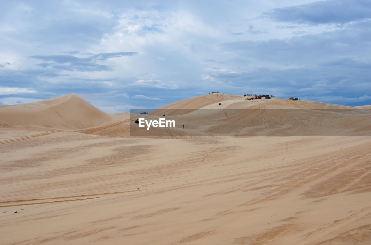 View of sand dunes in desert against cloudy sky