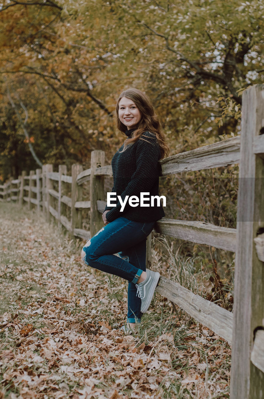 Portrait of smiling girl standing by wooden railing during autumn